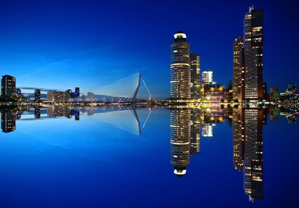 Beautiful night view of Rotterdam skyline with illuminated buildings and Erasmus Bridge reflection.
